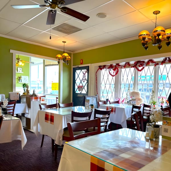 Interior of Royal Thai Orchid Restaurant with green walls, white tablecloths, and festive red and white decorations.