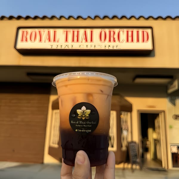 Hand holding a Thai iced tea with the Royal Thai Orchid restaurant sign in the background.
