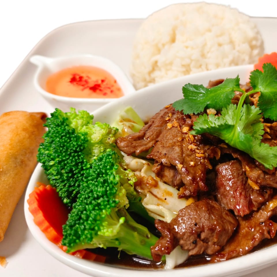 Thai beef dish with broccoli, carrots, rice, and a spring roll on a white plate.