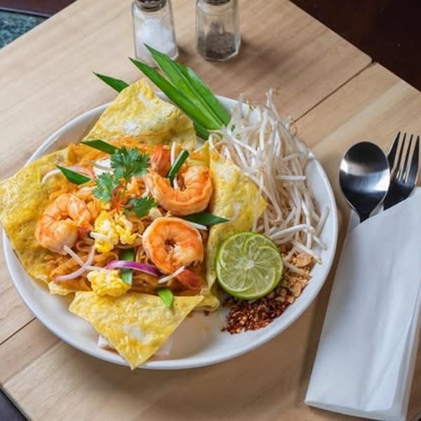 Royal Thai Orchid's Pad Thai with shrimp, bean sprouts, lime, and chili flakes on a wooden table.