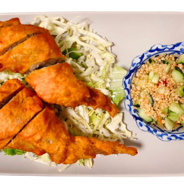 Crispy golden-brown fried chicken pieces on a bed of shredded cabbage, with a side of cucumber salad.