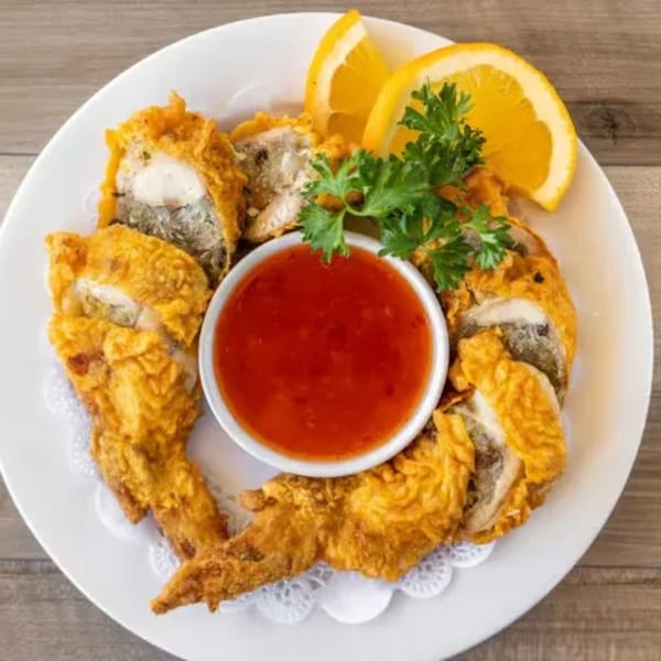 Crispy fried chicken wings with sweet chili sauce, orange slices, and parsley on a white plate.
