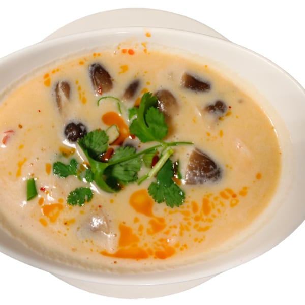 Creamy Thai soup with mushrooms, cilantro, and chili oil in a white bowl.