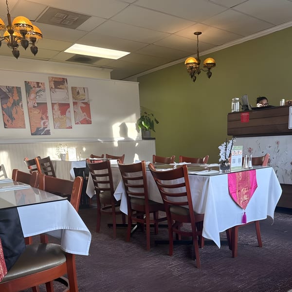 Interior of Royal Thai Orchid Restaurant with set tables, traditional art, and a person at the counter.