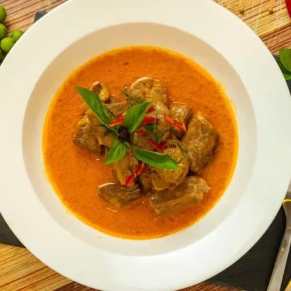 Royal Thai Orchid's red curry with beef, garnished with basil and chili, in a white bowl.