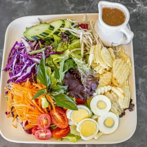 Colorful Thai salad with mixed greens, carrots, cabbage, tomatoes, eggs, chips, and dressing.